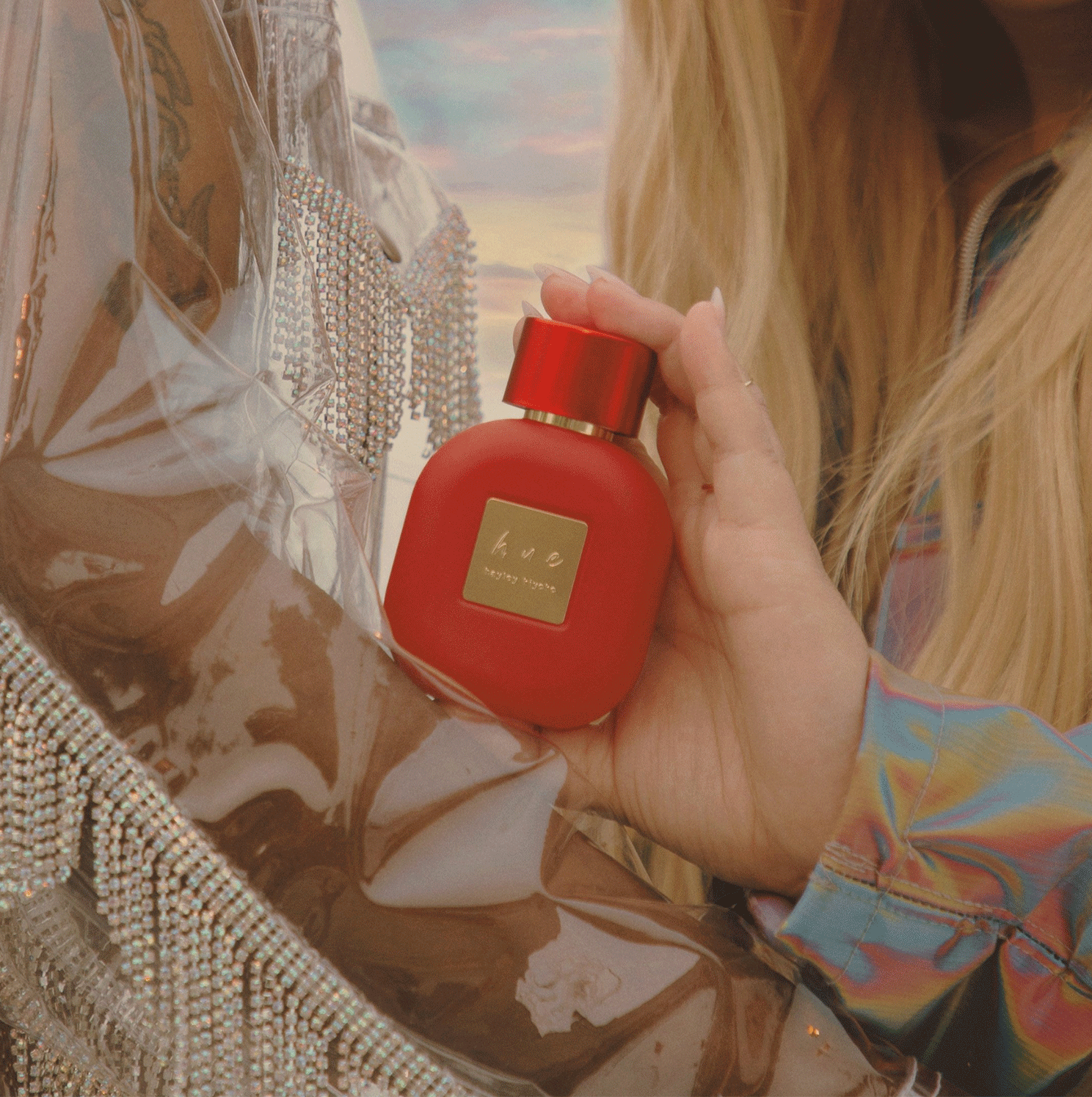 Close up photo of female celebrity, Hayley Kiyoko, holding her perfume in one hand.