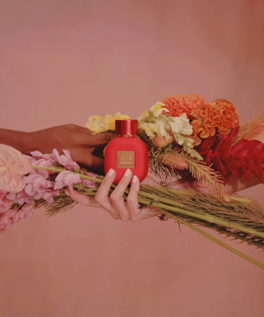 Two hands holding small bouquets of colorful flowers with best celebrity perfume being held on top of one of the bouquets.