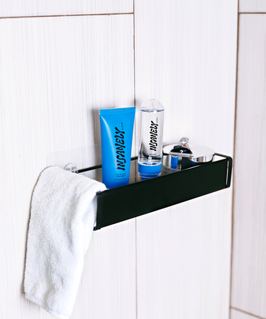 Best men's skincare products and a white towel placed on a black shelf that is hanging from a tiled shower wall.